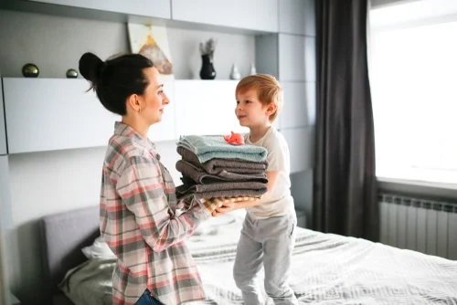 Mother and child folding clean laundry while cleaning and organizing a bedroom