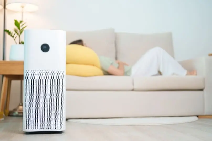 Modern air purifier in living room with person resting on sofa, showing are air purifiers worth it for clean indoor air
