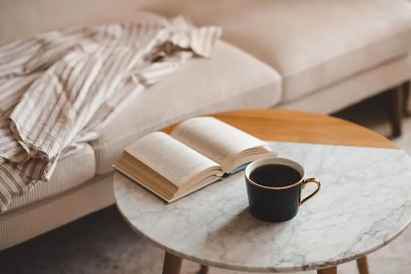 A cup of coffee and an open book on a table, relevant to how to get coffee out of carpet.