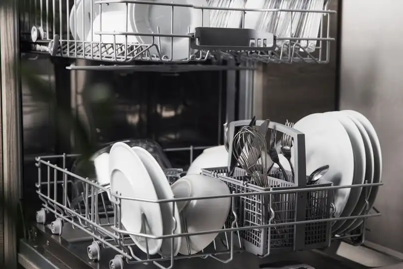 A fully loaded dishwasher rack with dishes and silverware, explaining how a dishwasher works.