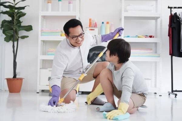 A smiling father and son mop a floor together, showing hacks working parents keep house clean