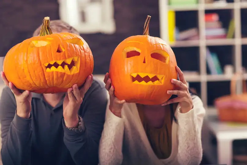 Two people hold carved jack-o'-lanterns over their faces, preceding the need for halloween cleaning.