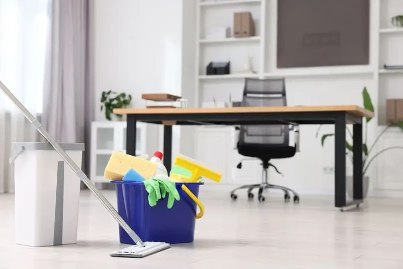 A mop and a blue bucket filled with cleaning supplies for office space, desk, and chair.