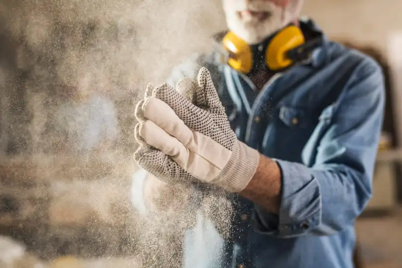 Worker wearing gloves surrounded by dust particles, illustrating how to clean up construction dust effectively
