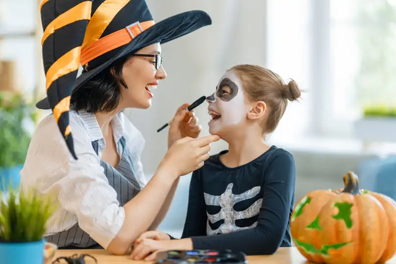 A mom applies skeleton Halloween makeup to her daughter's face, related to how to remove Halloween makeup out of fabric.