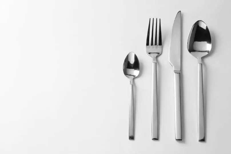 Four pieces of clean, shining silver cutlery (fork, knife, spoons) on a white background, suggesting how to clean silver.