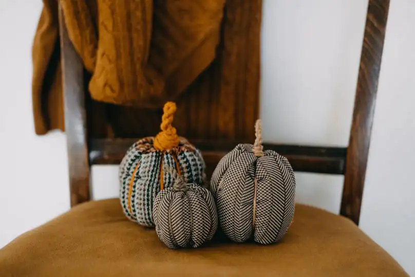 Three small, decorative fabric pumpkins sitting on a wooden chair, suggesting the cleaning of fabric dining chairs.