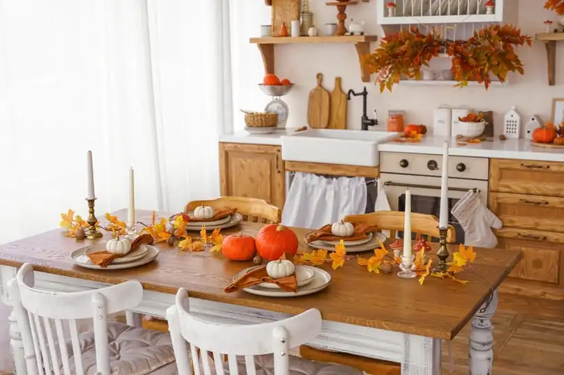 A kitchen decorated for fall with pumpkins and candles on the table, offering Thanksgiving kitchen organization tips.
