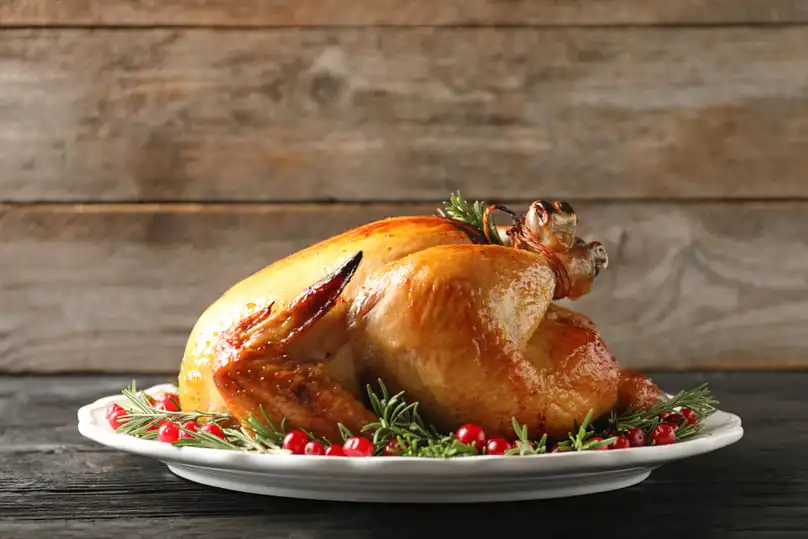 A glossy roasted turkey garnished with cranberries and rosemary, a source of turkey grease stain removal needs.