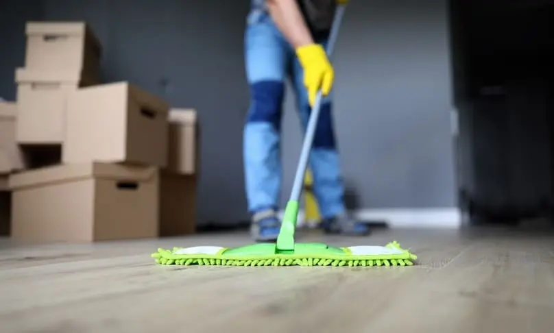 A person mops a floor near a stack of cardboard boxes, relating to move in cleaning service vs DIY.