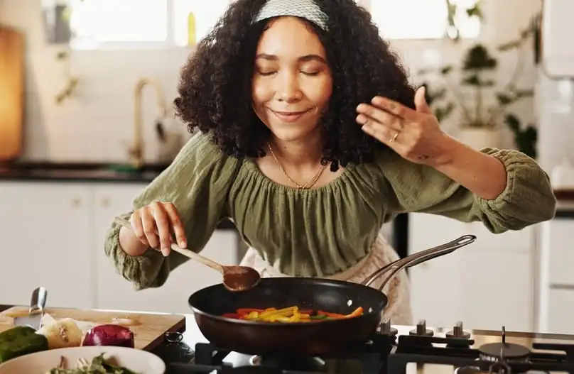 Woman cooking at home and smelling food, with tips on how do you get rid of cooking odors