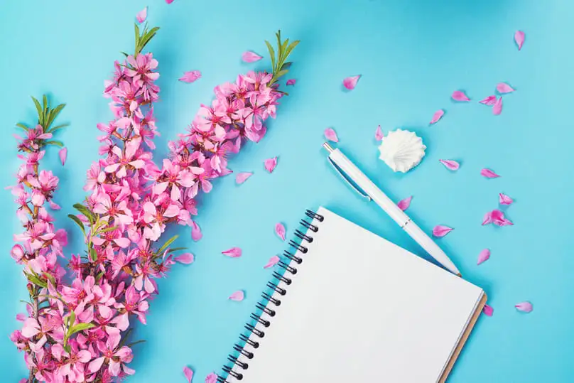 A notebook and pink blossoms, ready for your spring cleaning checklist tasks..
