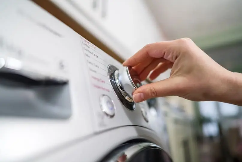 A hand turns a dial on a white laundry unit, showcasing the best way to clean a washing machine.