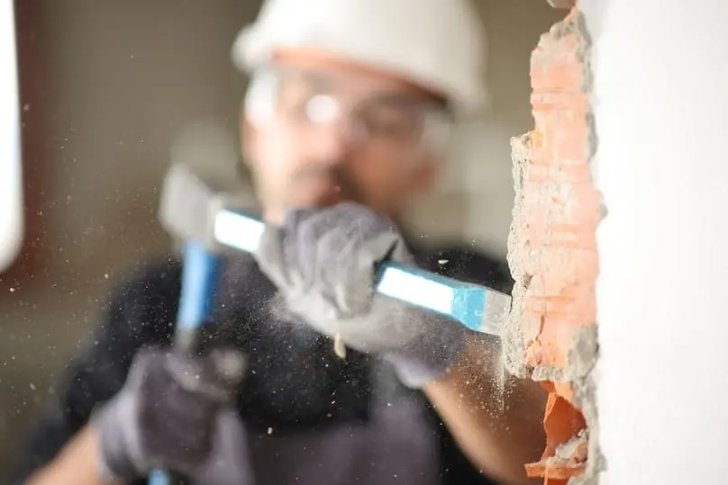 A worker breaking a brick wall, highlighting the need for construction dust control.