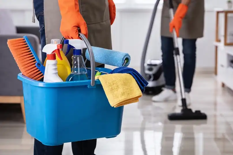 A person in gloves carries a blue bucket filled with the best cleaning tools for any home.