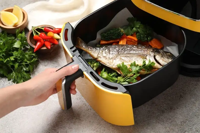A hand pulls out a yellow basket with cooked fish, showing how to clean air fryer units.