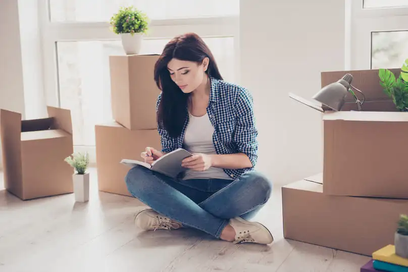 A woman takes notes amidst boxes, planning how to prepare for a move.
