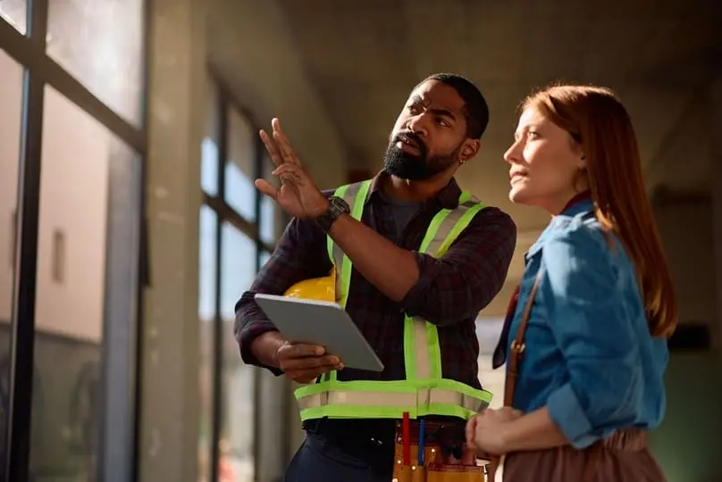 A builder points out window details to a client, preparing for a post-construction cleaning checklist.