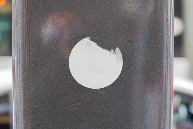 A torn white sticker on a dark surface shows the need for how to remove sticker residue.