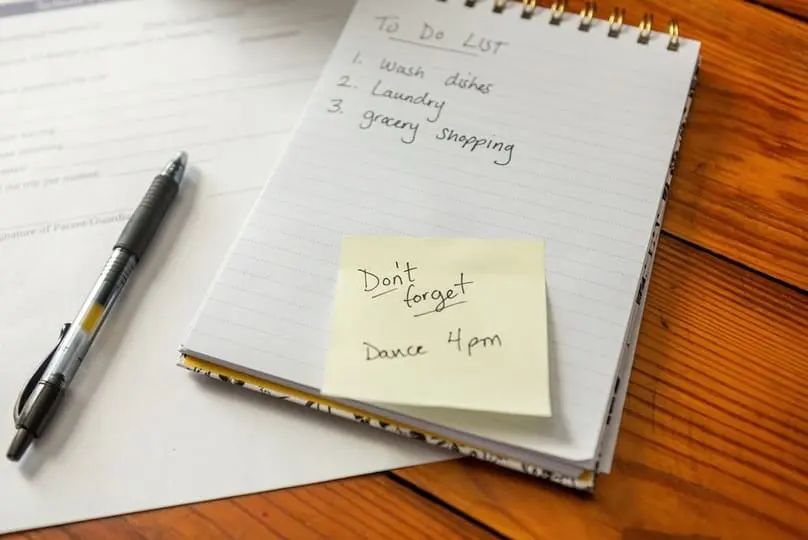 A pen and open notebook on a wooden table showing a to-do list of everyday chores.