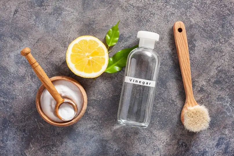 A bottle of vinegar, fresh lemon, and baking soda show why vinegar is good for cleaning.