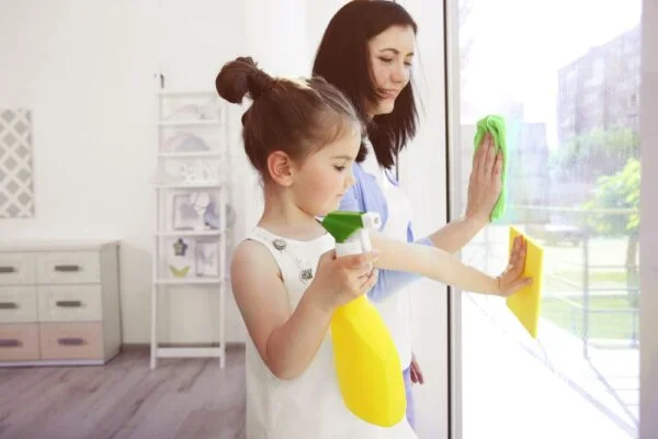 Woman and child cleaning a large window during routine house cleaning in a bright home