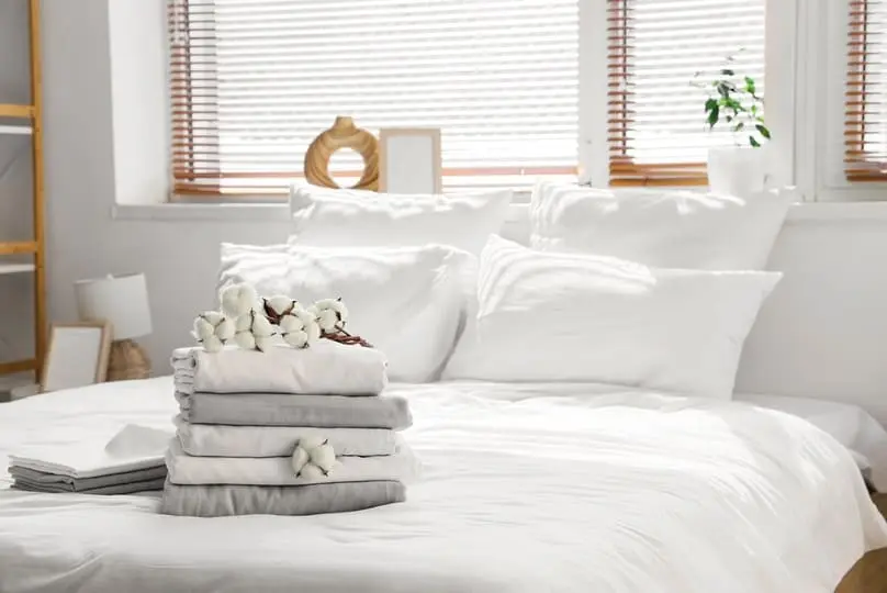 A neat stack of folded linens with cotton flowers highlights how often to wash sheets.
