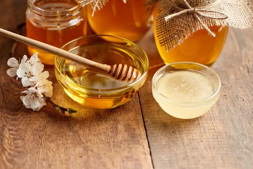 A wooden dipper resting in a glass bowl of golden honey shows how to remove honey stains.