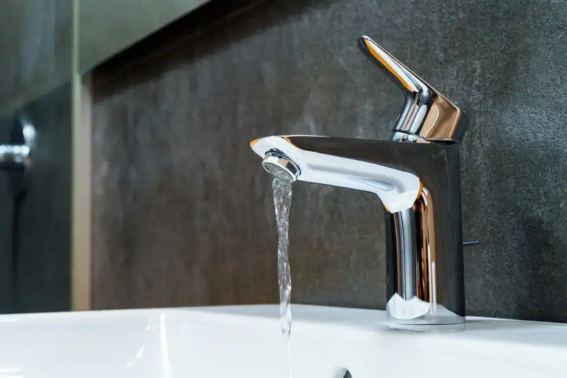 A sleek chrome faucet running clear water answers the question, why is my bath water yellow.